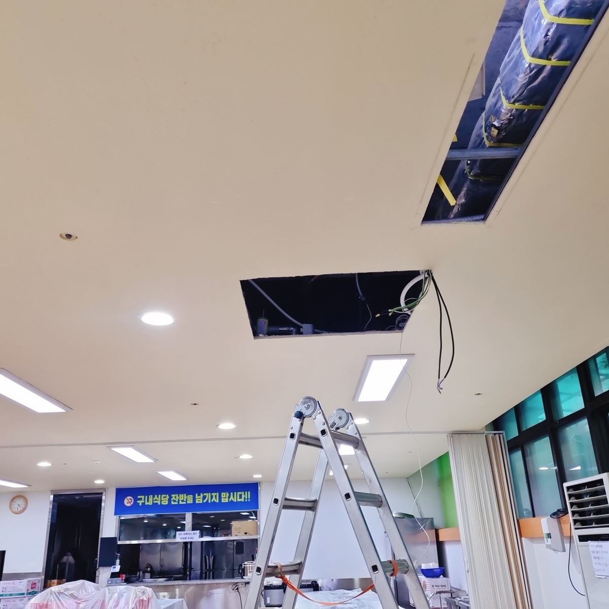 식탁을 비닐로 덮고 사다리를 세운 식당, 천장에 실내기 자리가 네모나게 뚫려 있다