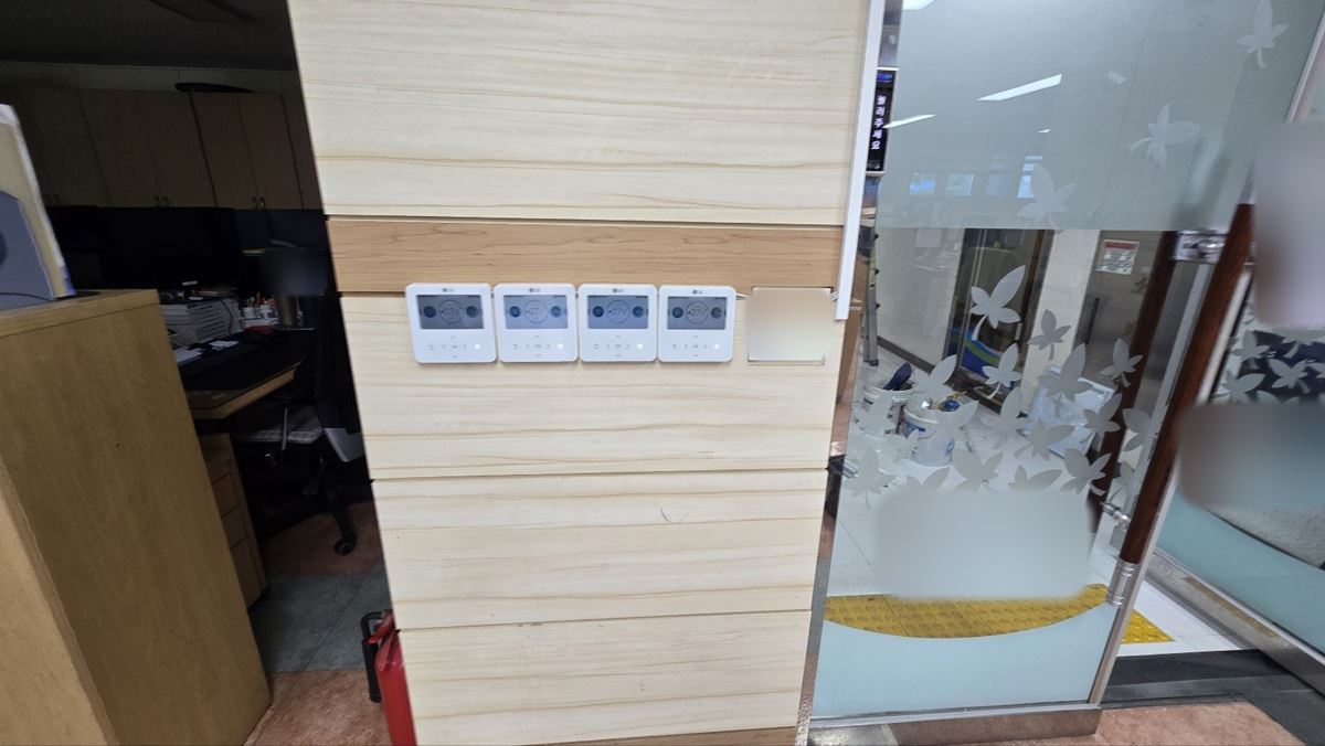나무 무늬 기둥 한 면에 나란히 붙은 흰색 룸컨트롤러 4개와 오른쪽 유리문